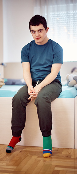Young man wears different socks while sitting on bed.